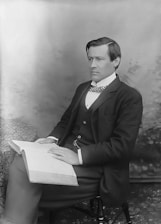 A high-quality photo of a man in a formal suit holding a book inside a modern office setting.