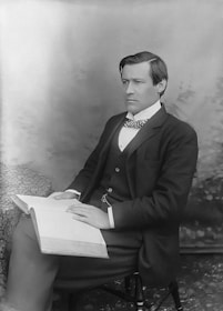 A high-quality photo of a man in a formal suit holding a book inside a modern office setting.