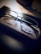 A pair of eyeglasses rests on a textured glasses case on a dark, reflective surface. The lighting creates a contrast, highlighting the clarity of the lenses against the muted tones of the background.