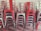 A stack of metal chairs arranged in an orderly manner, with alternating colors of red and metallic gray. The chairs are placed against a neutral-colored wall, and their industrial design is evident.