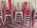 A stack of metal chairs arranged in an orderly manner, with alternating colors of red and metallic gray. The chairs are placed against a neutral-colored wall, and their industrial design is evident.