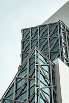 A modern architectural structure with intersecting steel beams and large glass windows. The design features triangular and rectangular elements, giving the building a geometric appearance.