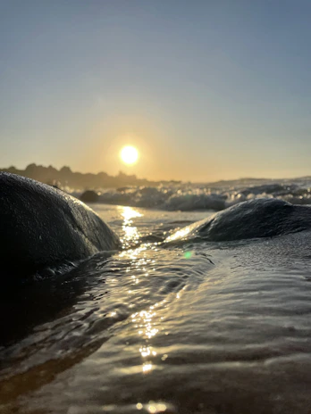 Close-up of gentle waves lapping against smooth stones, bathed in warm evening light.