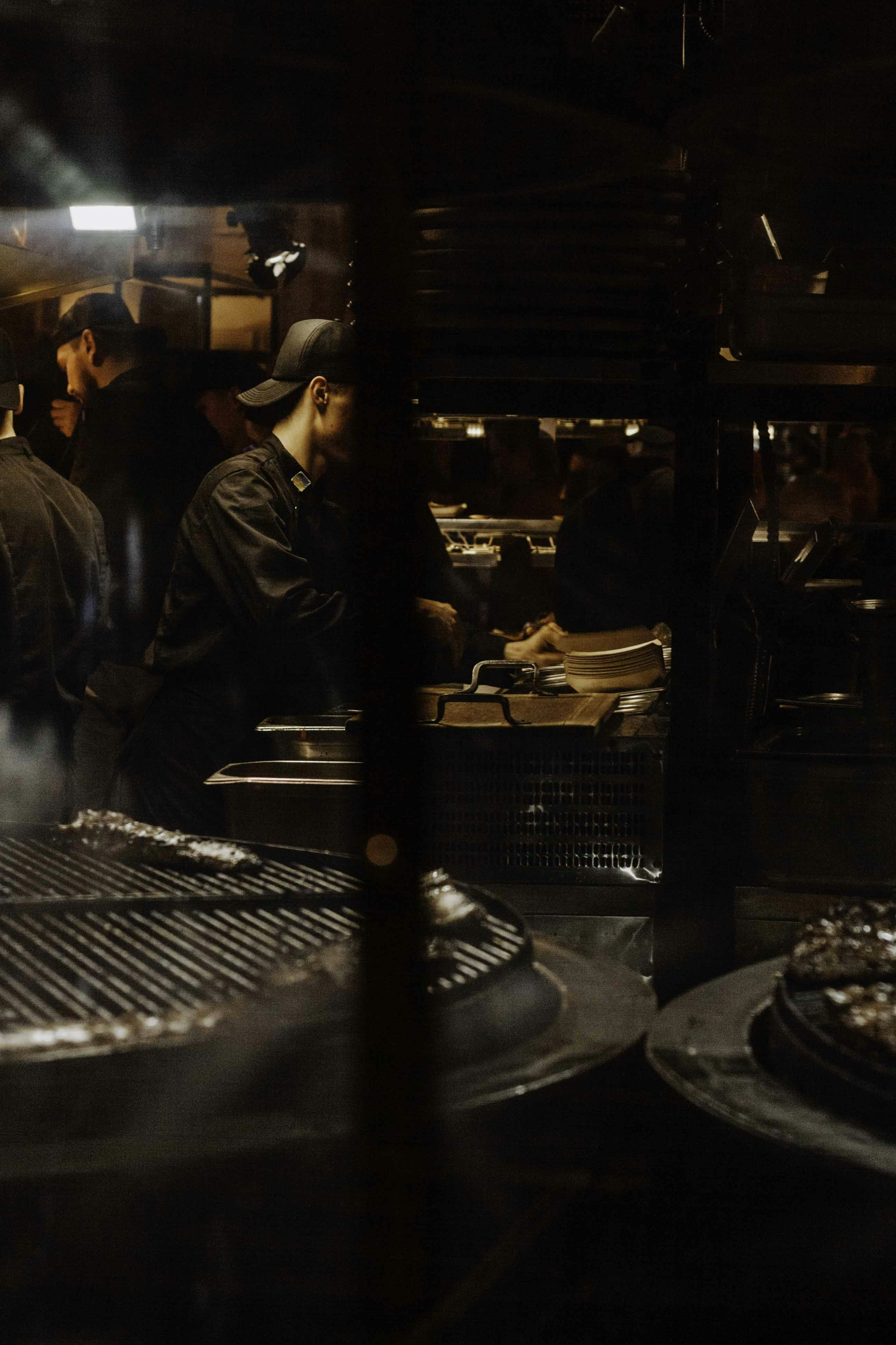 Restaurant team gathered in dark atmospheric dining room, warm amber light, professional setting, group of chefs and servers in black uniforms
