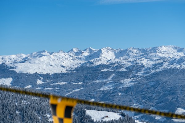 A snowy range across a valley with a ski lift bar in the foreground under a blue sky