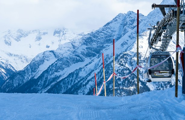 A lift cabin and orange-banded piste poles beside a snowy peak