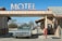 A vintage car is parked under the awning of an old-fashioned motel, with a large sign reading 'MOTEL' on top. The structure features stone walls and a small payphone is visible on the right side. The setting is in a desert landscape, with dry bushes and a clear blue sky in the background.