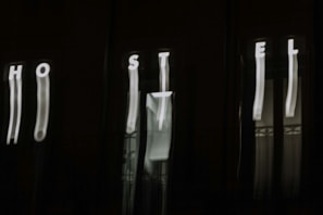 The image features a dark background with blurry, vertically elongated white letters spelling out 'HOSTEL'. The letters appear to be on an illuminated sign, but due to the blur, they are distorted and stretched.