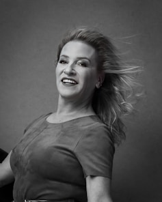 Portrait of a smiling woman in a black and orange branded shirt standing in a modern short-term rental living room.