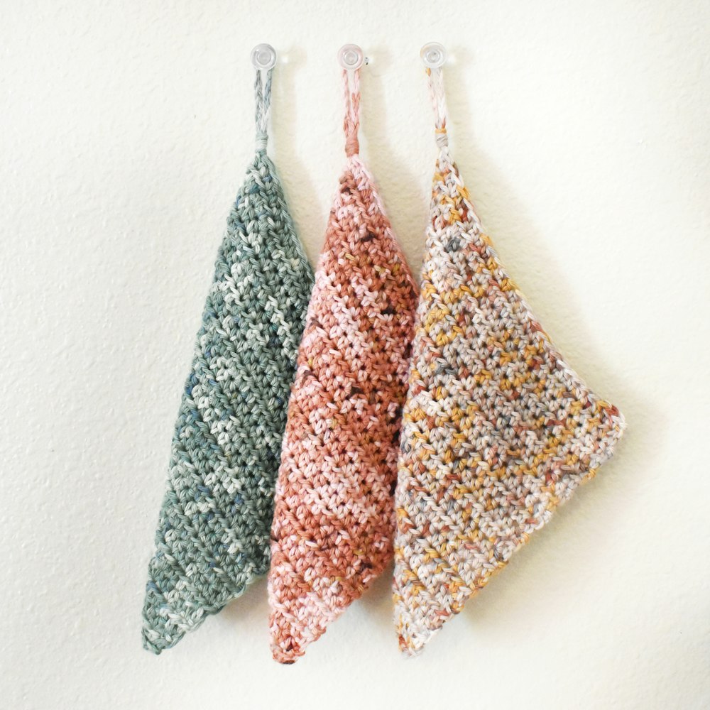 three pieces of crocheted fabric hanging from hooks