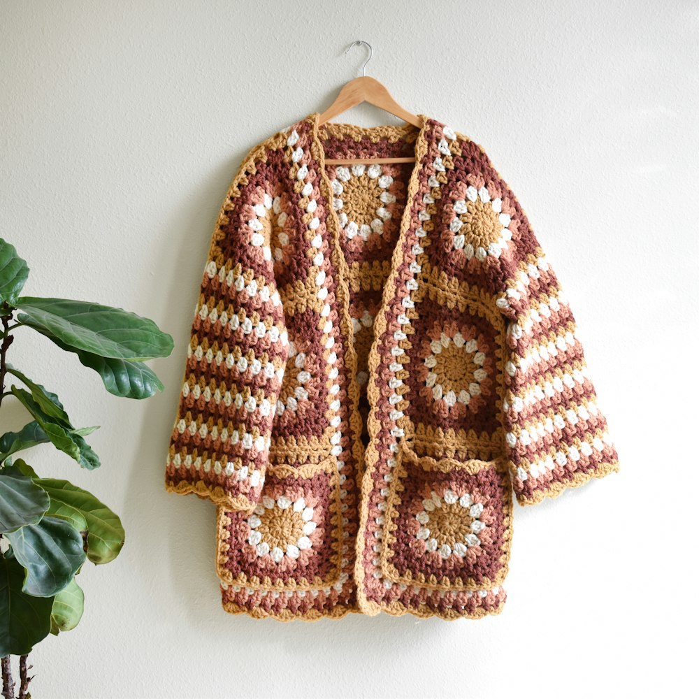 a crocheted jacket hanging on a wall next to a potted plant