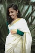 A woman wearing a colorful traditional saree, smiling in a bright outdoor setting.