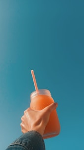 A cheerful person holding a bottle of fresh juice in a sunny kitchen.