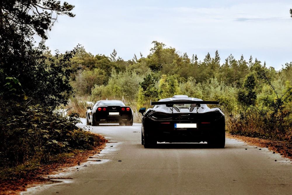 a couple of cars driving down a road next to a forest