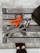 A wooden bench with metal bolts is viewed from above, holding fitness-related items including a jump rope with orange handles, an elastic exercise band, and a keychain with keys. The pavement and a pair of feet in black shoes are partially visible.