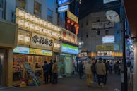 The exterior of Genba Street at dusk, glowing warmly with inviting storefronts and street lamps.