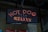 An LED sign displaying the words 'HOT DOG' in red lights with decorative elements represented by small dots. The sign is mounted on a background of pegboard and brick wall.