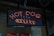 An LED sign displaying the words 'HOT DOG' in red lights with decorative elements represented by small dots. The sign is mounted on a background of pegboard and brick wall.