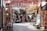 A narrow, cobblestone street lined with wooden storefronts and outdoor seating. Turkish flags hang overhead, adding a festive and cultural touch. People are seated at tables, engaging in conversation or relaxing, creating a lively yet cozy atmosphere.