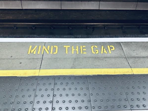 a sign that says mind the gap on the sidewalk