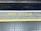 A train platform edge with a warning message painted on the ground in yellow that reads 'Mind the Gap'. The area consists of a textured surface with dotted patterns and a distinct yellow line indicating safety boundaries.