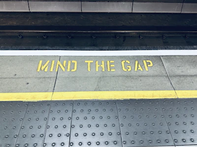a sign that says mind the gap on the sidewalk