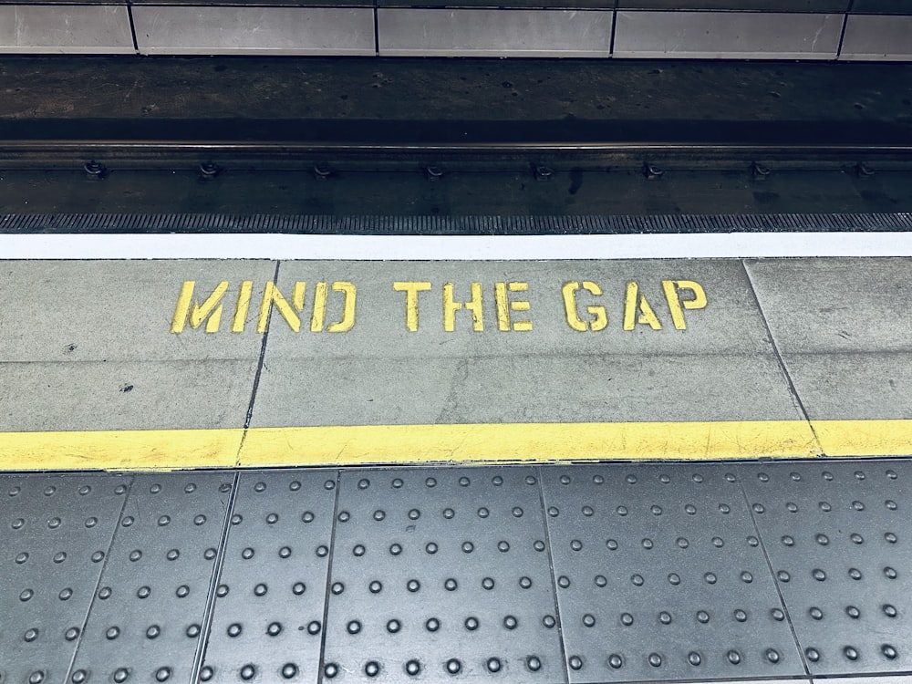 a sign that says mind the gap on the sidewalk