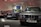 Several classic BMW cars are on display in a showroom. The cars are positioned side by side, showcasing their vintage design. A red car and an engine are visible in the background along with several colorful car panels mounted on the wall.