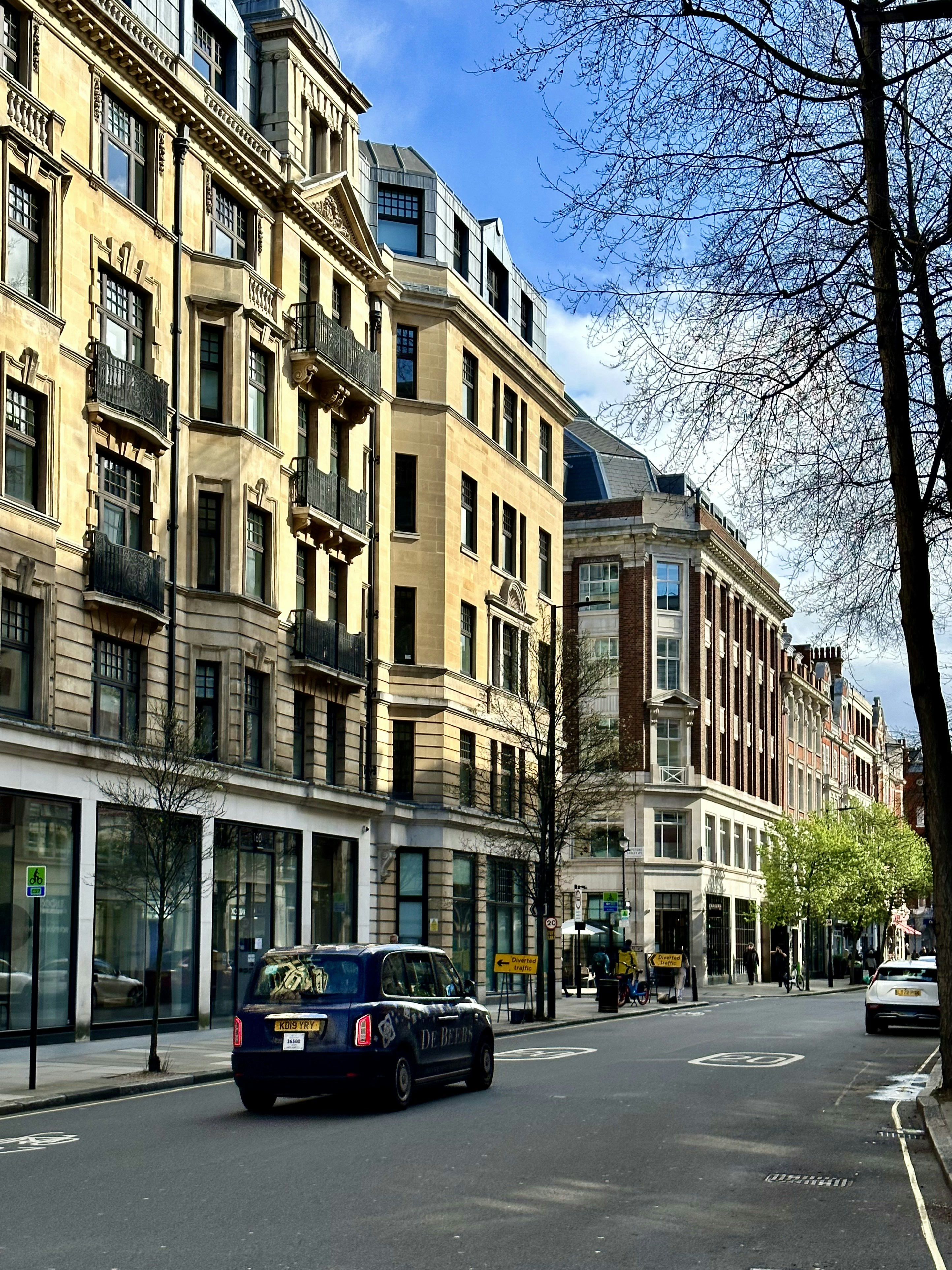 A car driving down a street next to tall buildings photo Free Londra