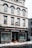 A multi-story building with a white facade and black accents houses a business named Andersons, which offers butcher and takeaway services. Large display windows show some indoor plants and the entrance is centrally located. Snow is piled up on the sidewalk in front of the building.