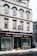 A multi-story building with a white facade and black accents houses a business named Andersons, which offers butcher and takeaway services. Large display windows show some indoor plants and the entrance is centrally located. Snow is piled up on the sidewalk in front of the building.