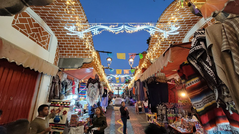 A vibrant city street bustling with people and colorful market stalls during golden hour.