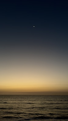 A close-up of a glowing crescent moon over a calm sea.