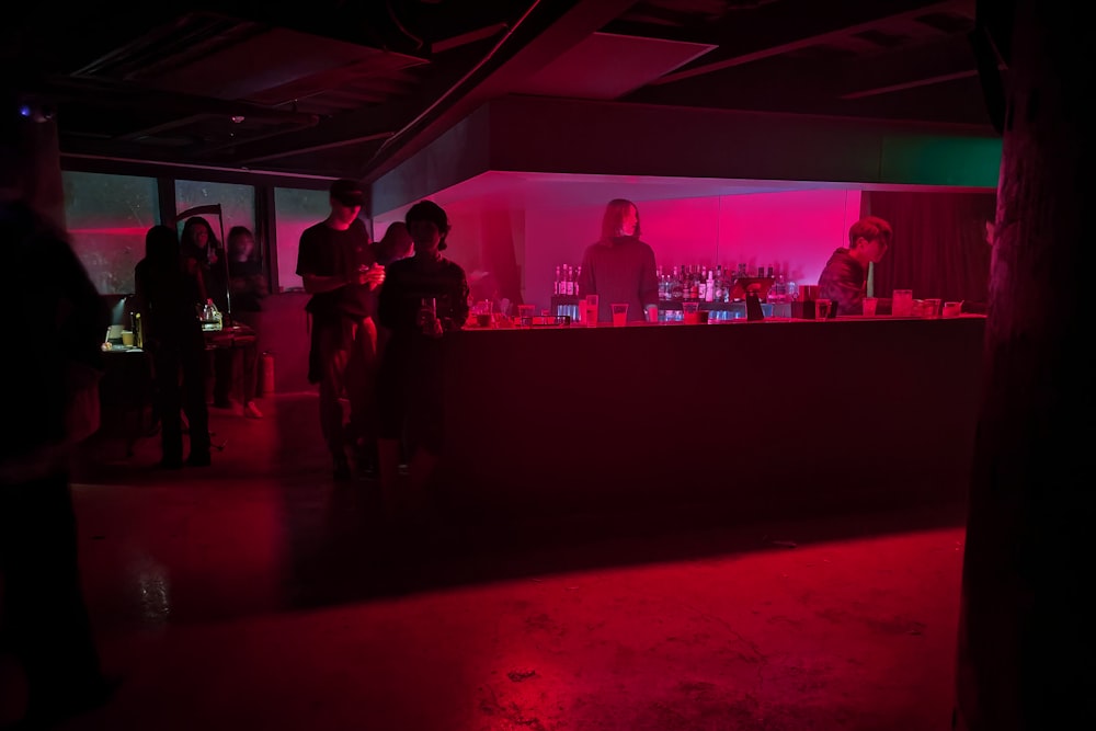 a group of people standing around a bar in a dark room