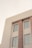 A section of an architectural structure displaying a minimalist, modern design with clean lines and symmetrical windows. The facade includes several large, rectangular windows with metal frames and vertical fluted columns that add a classic touch. The color palette is mostly neutral, with soft beige tones.