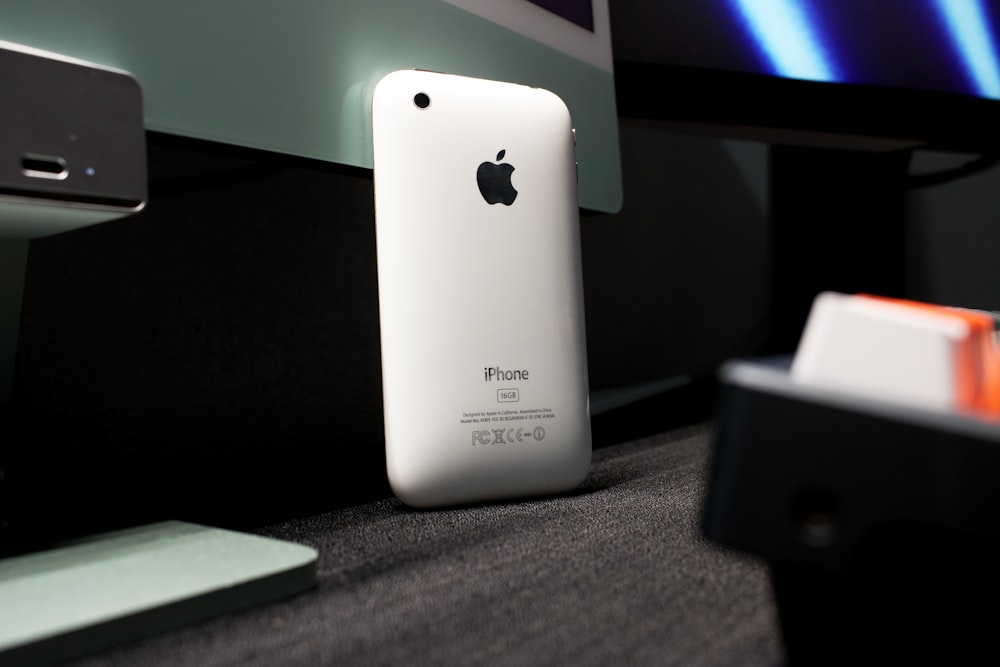 Un iPhone blanco sentado encima de un escritorio junto a un monitor