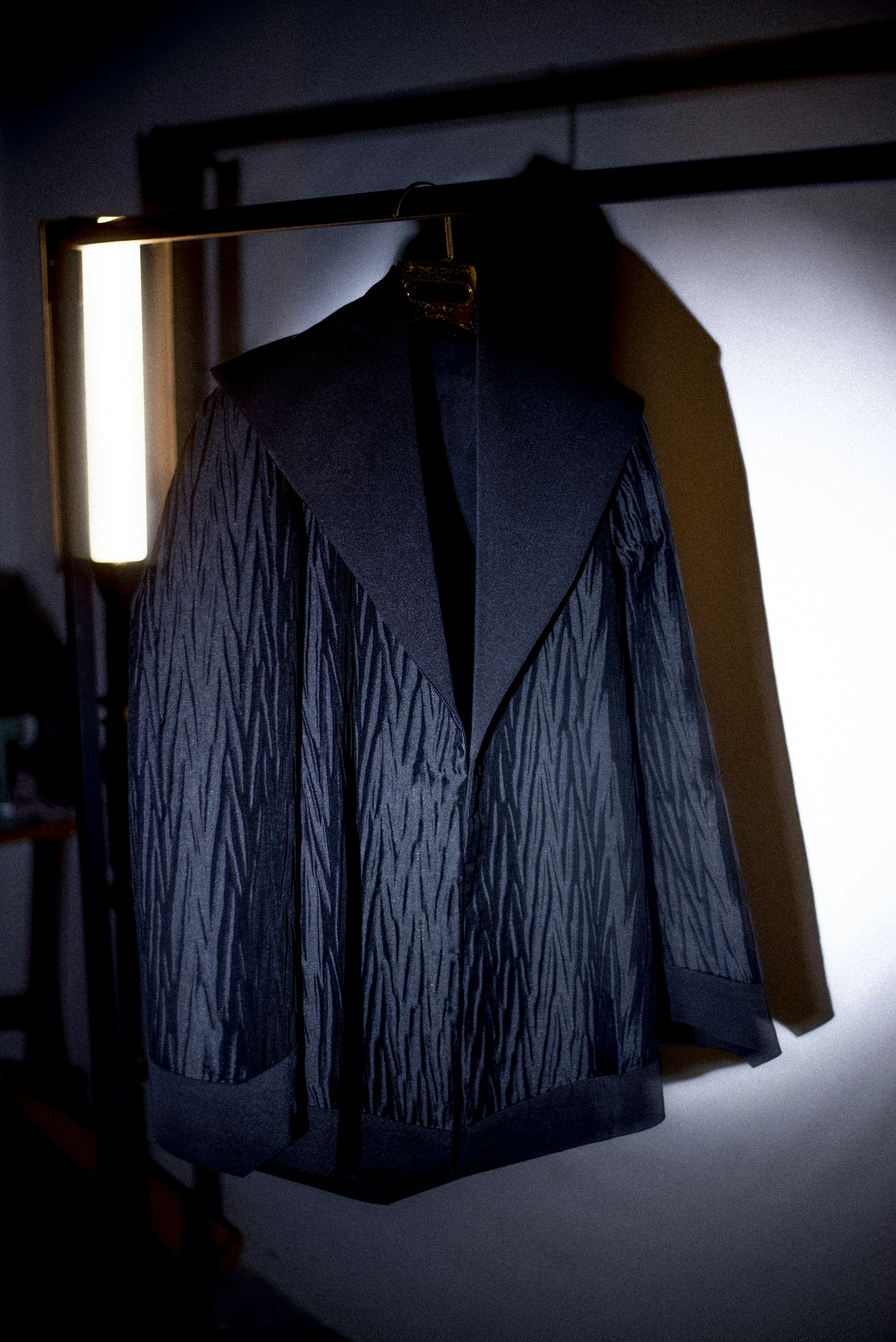 Dark leather and technical jacket hanging on rack in dimly lit studio