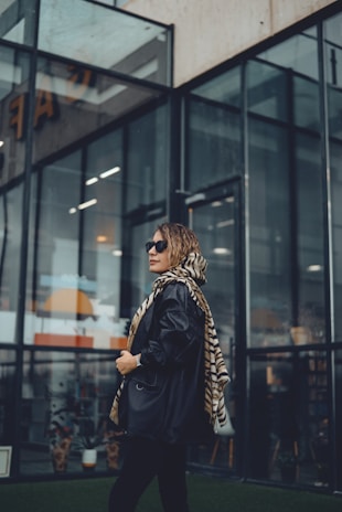 Model adjusting a scarf while standing near a modern glass building, showcasing layered city style.