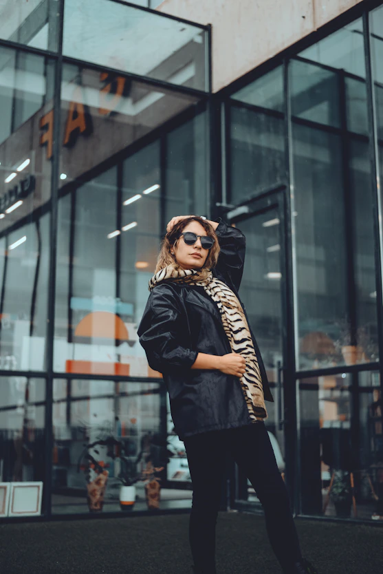 a woman standing outside of a building wearing a black jacket and leopard print scarf