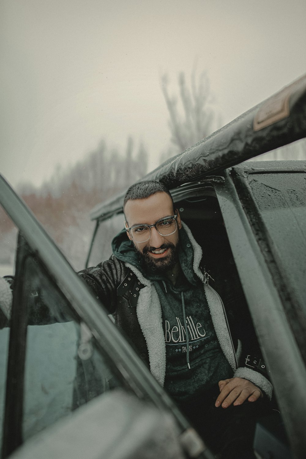 a man with a beard and glasses sitting in the driver's seat of a