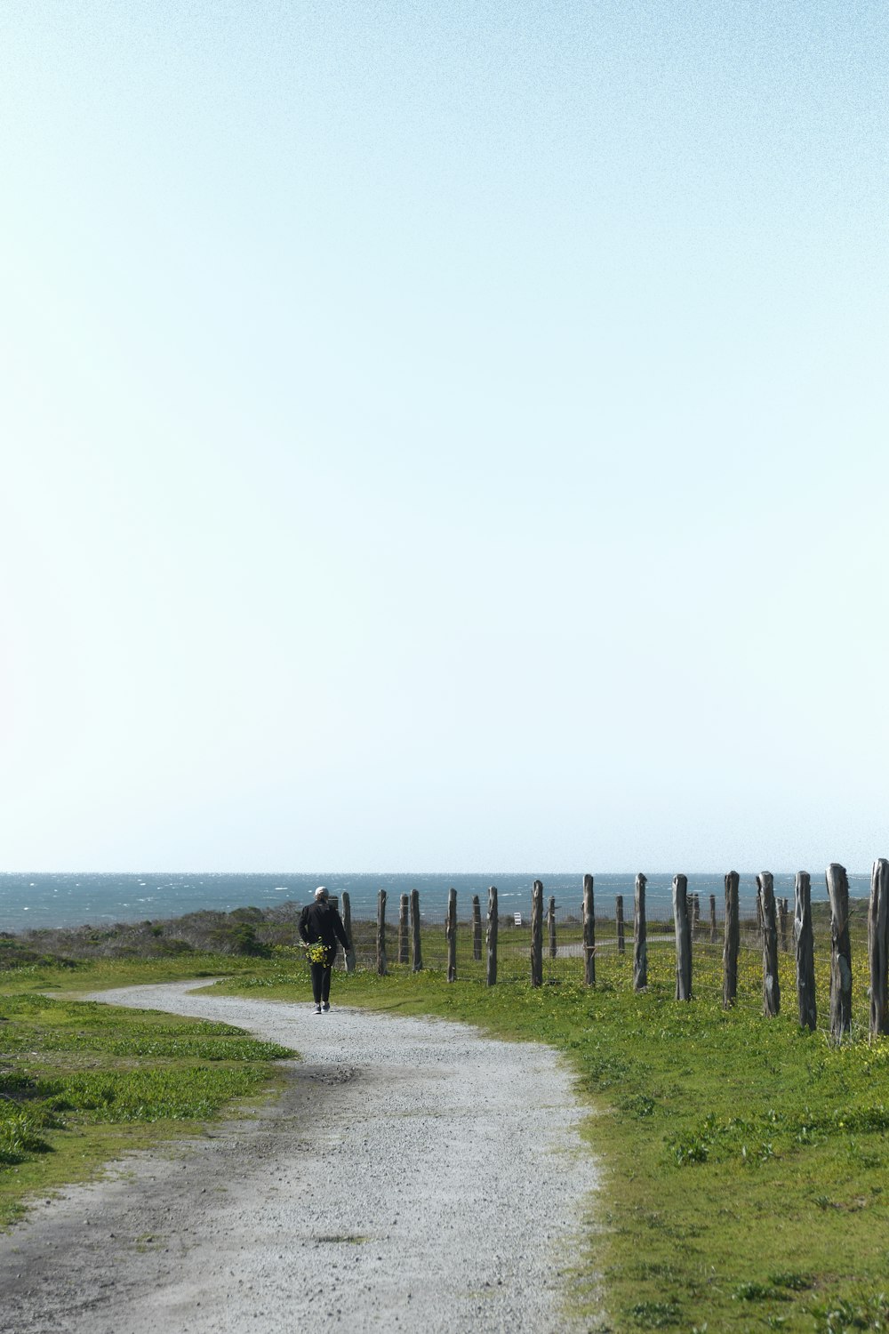 a person walking down a dirt road next to a fence