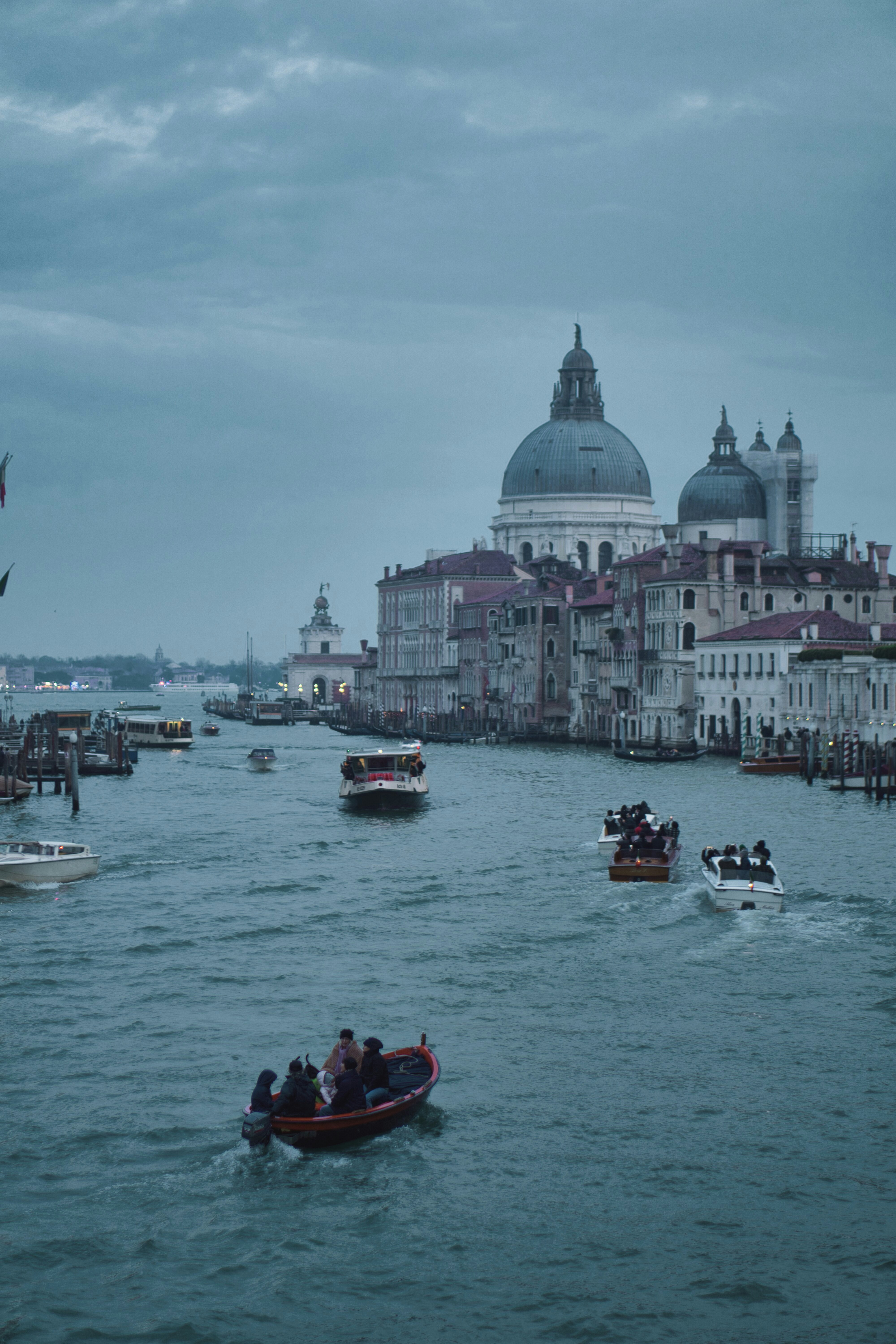 a group of boats traveling down a river next to tall buildings