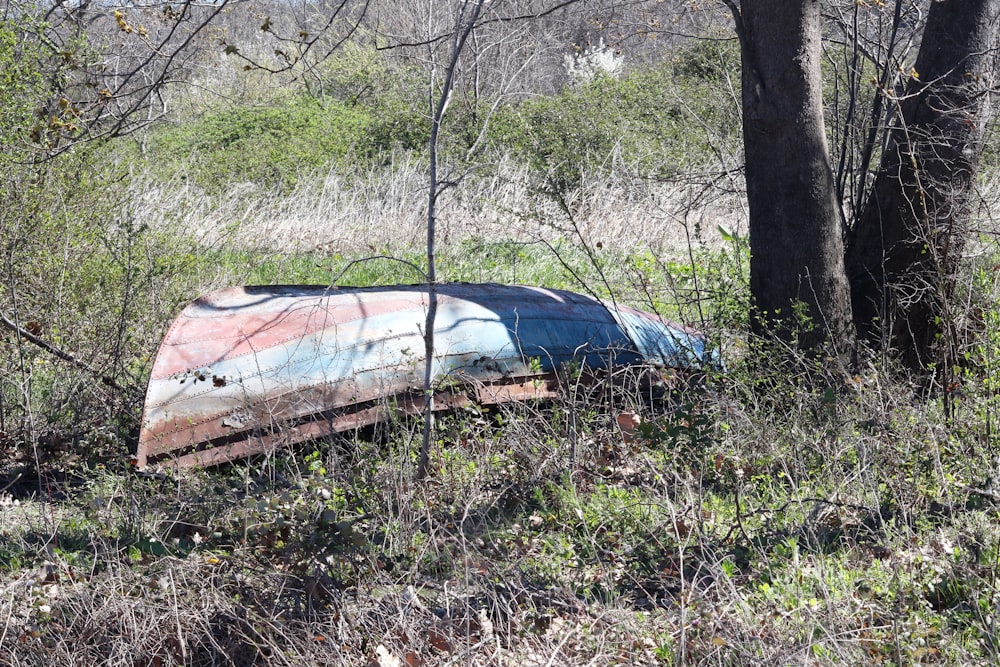 a rusted out boat sitting in the middle of a forest