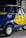 A small vintage car with a vibrant blue and yellow paint job, featuring the logo of a well-known airline company on its side. The car has a distinctive curved design with chrome accents, round headlights, and small tires. It is parked indoors, likely in a showroom or museum.