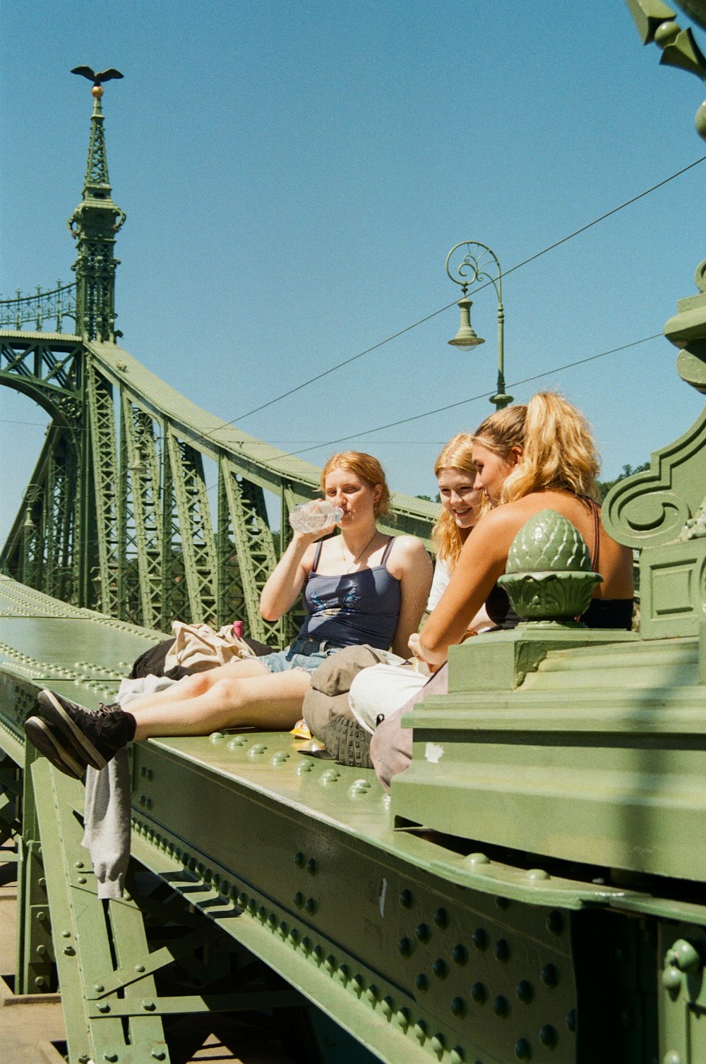 three women sitting on a bridge looking at something
