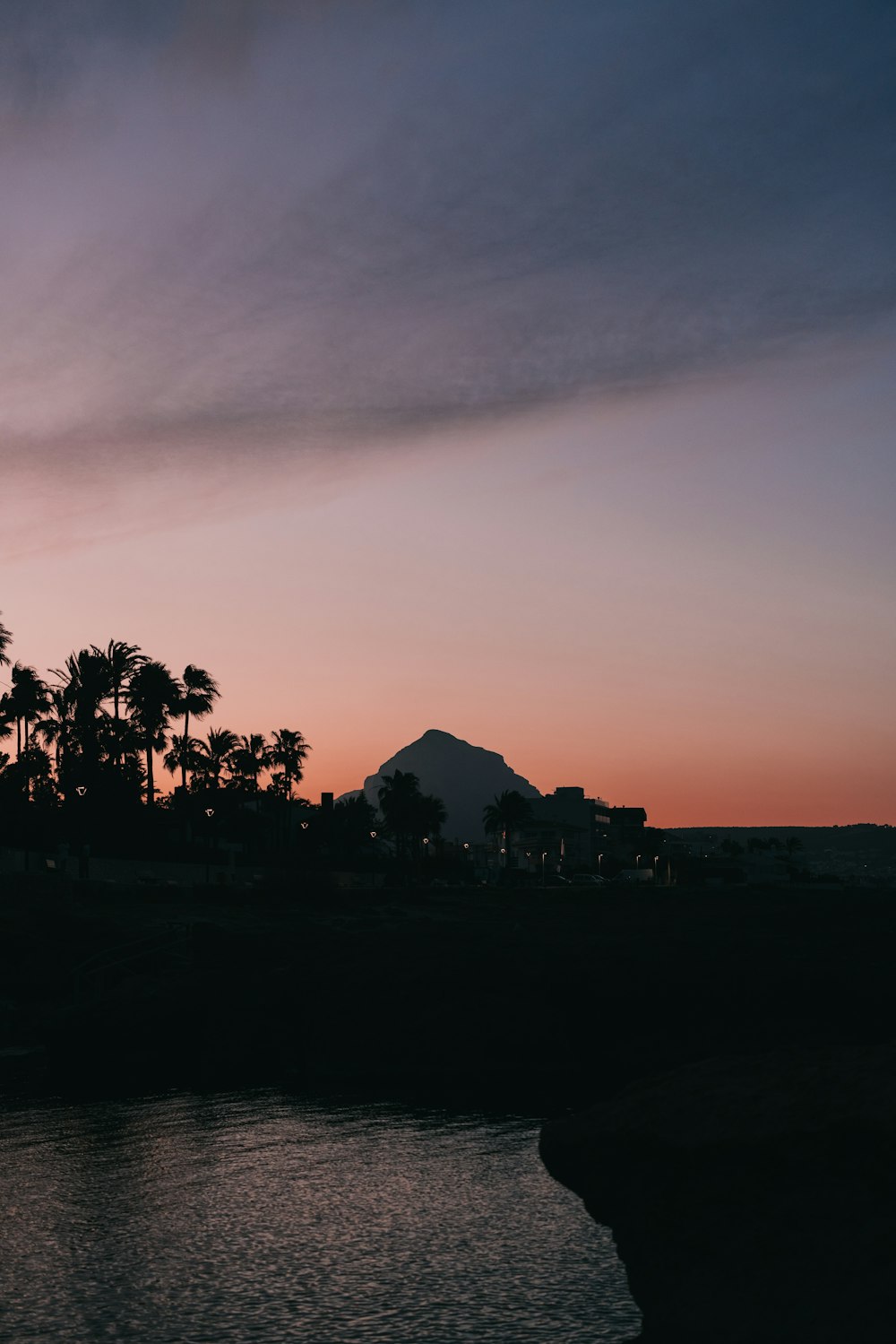 a sunset with palm trees and a mountain in the background