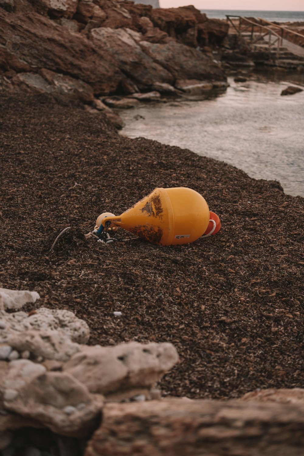 a yellow buoy laying on top of a rocky beach