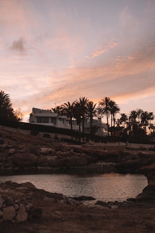 A modern beachfront condominium complex at sunset with palm trees swaying.