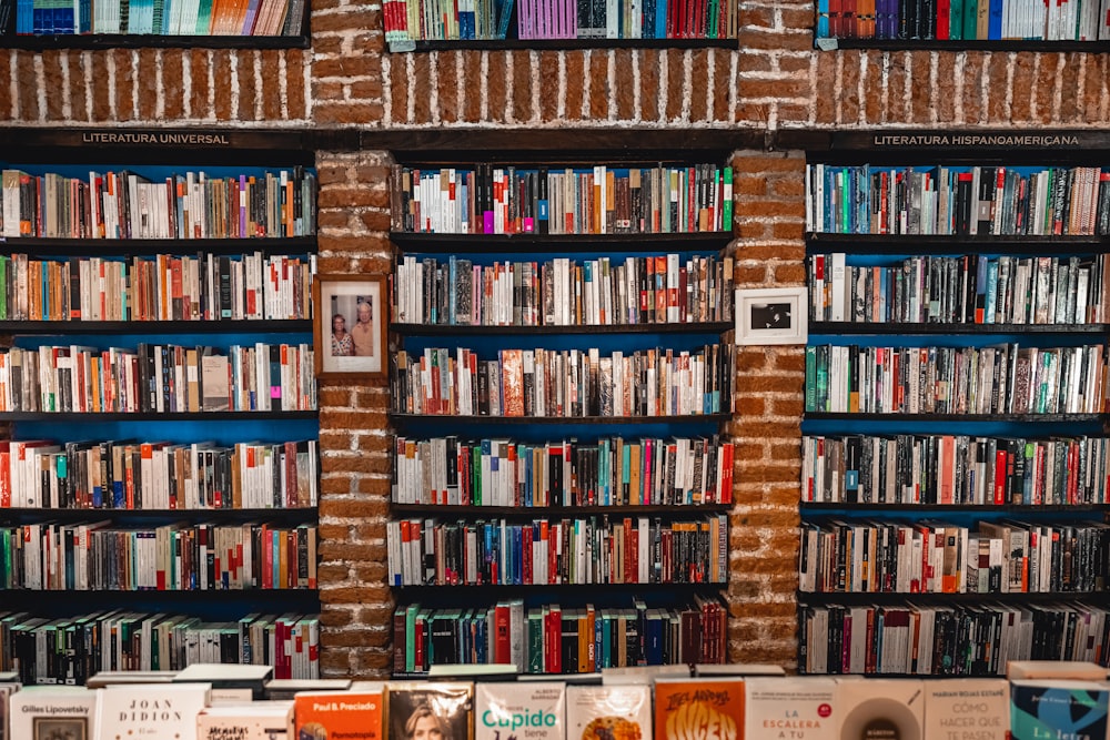 Una estantería llena de muchos libros junto a una pared de ladrillos