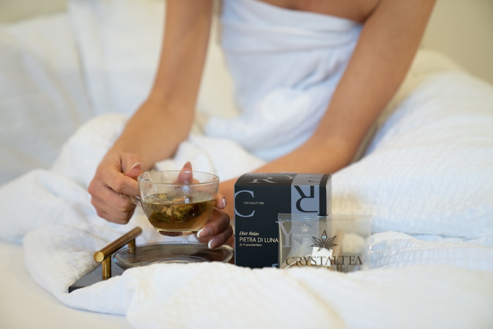 a person sitting on a bed holding a glass